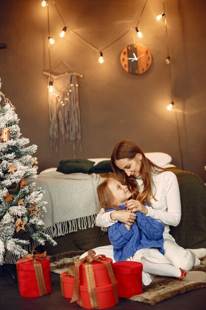 Personas que se preparan para Navidad. Madre jugando con su hija. La familia está descansando en una sala festiva. Niño con un suéter azul.