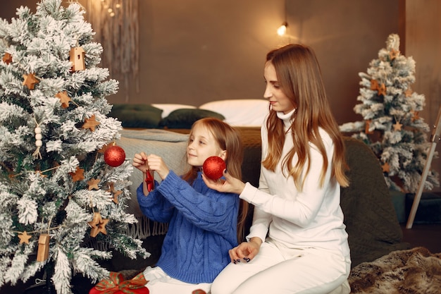 Personas que se preparan para Navidad. Madre jugando con su hija. La familia está descansando en una sala festiva. Niño con un suéter azul.