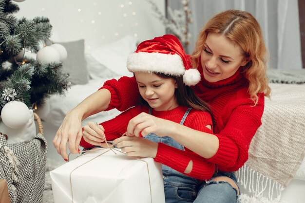 Personas que se preparan para Navidad. Madre jugando con su hija. La familia está descansando en una sala festiva. Niño con un suéter rojo.