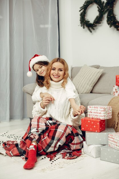 Personas que se preparan para Navidad. Madre jugando con su hija. La familia está descansando en una sala festiva. Niño con un suéter rojo.