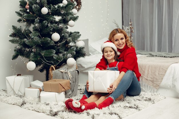 Personas que se preparan para Navidad. Madre jugando con su hija. La familia está descansando en una sala festiva. Niño con un suéter rojo.