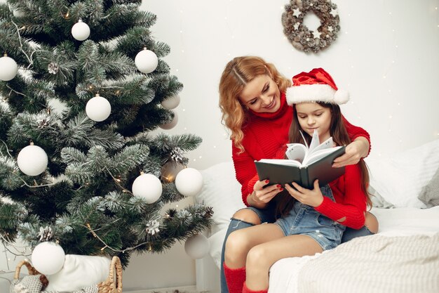 Personas que se preparan para Navidad. Madre jugando con su hija. La familia está descansando en una sala festiva. Niño con un suéter rojo.