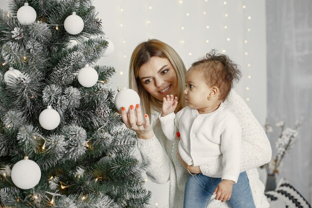 Personas que se preparan para Navidad. Madre jugando con su hija. La familia está descansando en una sala festiva. Niño en un suéter suéter.