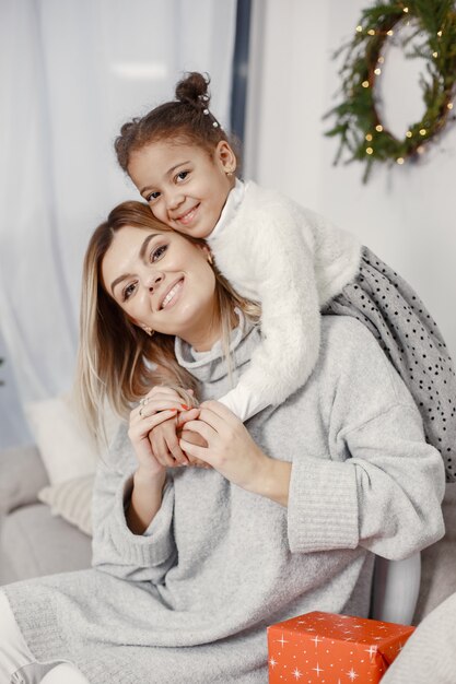 Personas que se preparan para Navidad. Madre jugando con su hija. La familia está descansando en una sala festiva. Niño en un suéter suéter.