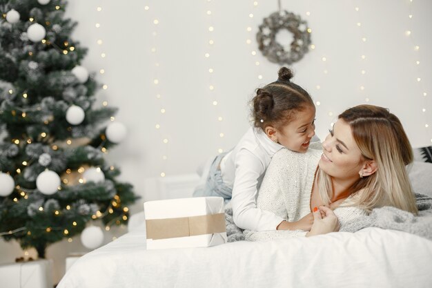 Personas que se preparan para Navidad. Madre jugando con su hija. La familia está descansando en una sala festiva. Niño en un suéter suéter.