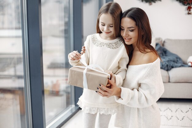 Personas que se preparan para la Navidad. Madre jugando con su hija. Familia de pie junto a la ventana. Niña con un vestido blanco.