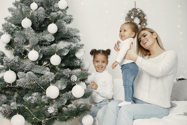 Personas que se preparan para Navidad. Madre jugando con sus hijas. La familia está descansando en una sala festiva. Niño en un suéter suéter.