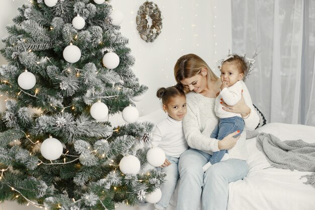 Personas que se preparan para Navidad. Madre jugando con sus hijas. La familia está descansando en una sala festiva. Niño en un suéter suéter.