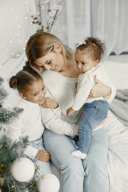 Personas que se preparan para Navidad. Madre jugando con sus hijas. La familia está descansando en una sala festiva. Niño en un suéter suéter.