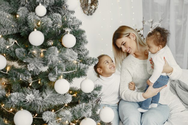 Personas que se preparan para Navidad. Madre jugando con sus hijas. La familia está descansando en una sala festiva. Niño en un suéter suéter.