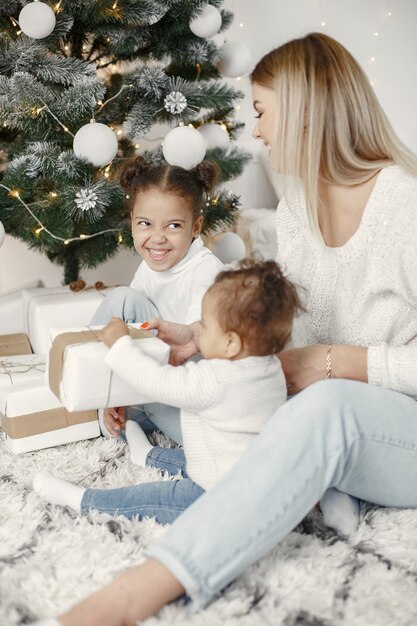 Personas que se preparan para Navidad. Madre jugando con sus hijas. La familia está descansando en una sala festiva. Niño en un suéter suéter.