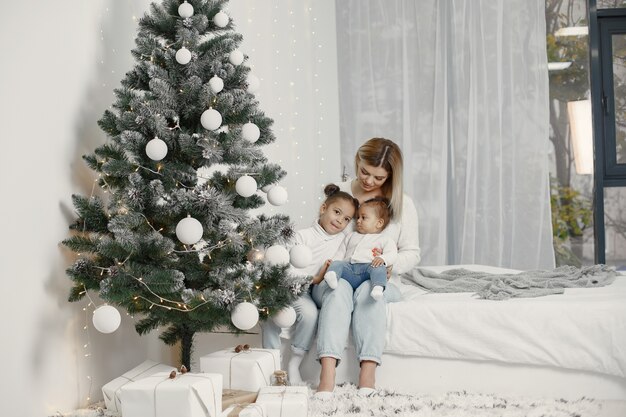 Personas que se preparan para Navidad. Madre jugando con sus hijas. La familia está descansando en una sala festiva. Niño en un suéter suéter.