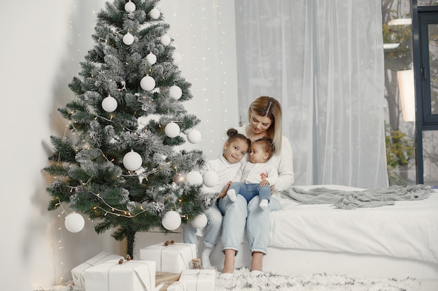 Personas que se preparan para Navidad. Madre jugando con sus hijas. La familia está descansando en una sala festiva. Niño en un suéter suéter.