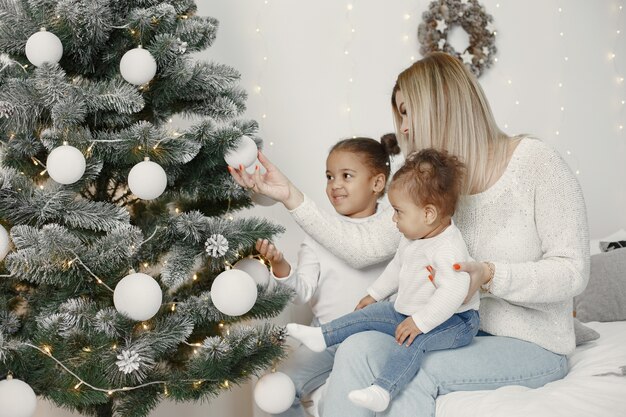 Personas que se preparan para Navidad. Madre jugando con sus hijas. La familia está descansando en una sala festiva. Niño en un suéter suéter.