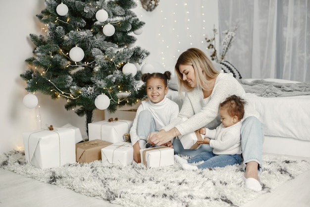 Personas que se preparan para Navidad. Madre jugando con sus hijas. La familia está descansando en una sala festiva. Niño en un suéter suéter.