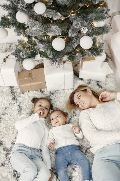 Personas que se preparan para Navidad. Madre jugando con sus hijas. La familia está descansando en una sala festiva. Niño en un suéter suéter.