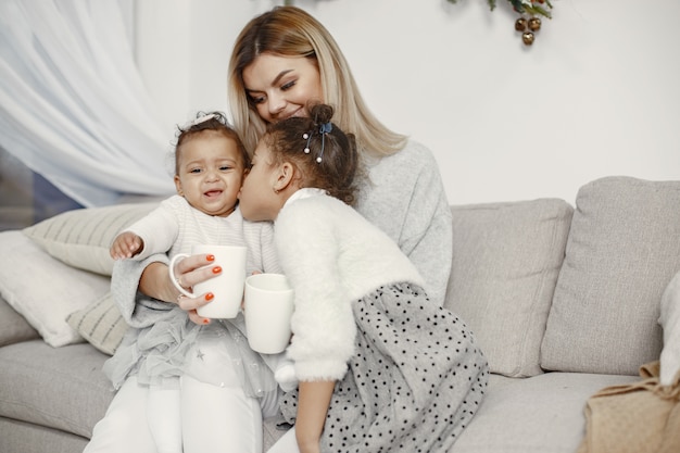 Personas que se preparan para Navidad. Madre jugando con sus hijas. La familia está descansando en una sala festiva. Niño en un suéter suéter.