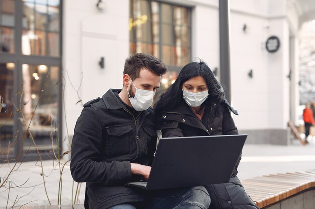 Las personas que usan una máscara protectora sentado en una ciudad con una computadora portátil