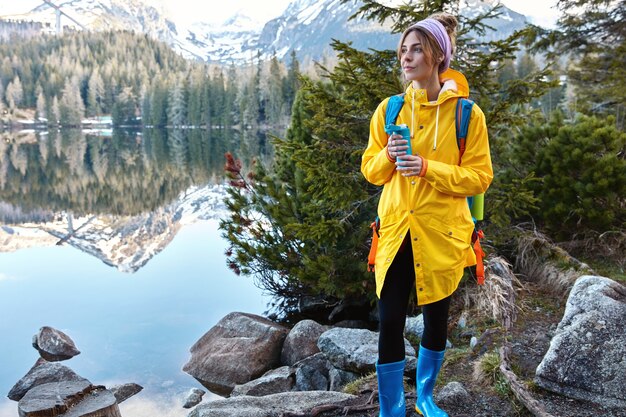 Personas, recreación, ocio, concepto de estilo de vida. Mujer pensativa en impermeable amarillo, botas de goma