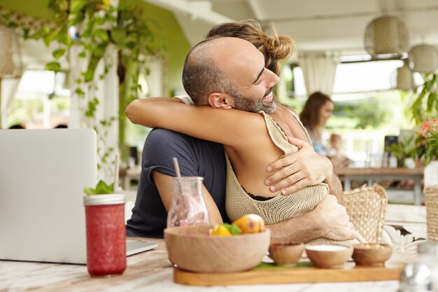 Personas y relaciones. Feliz pareja inventando después de una gran pelea, abrazándose mientras almuerza en el café.