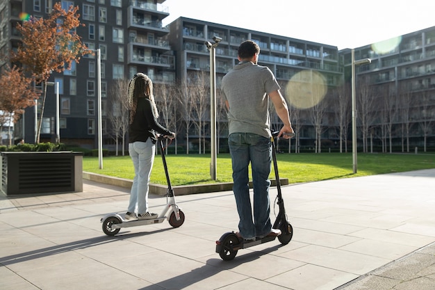 Personas de tiro completo que viajan con scooters eléctricos.