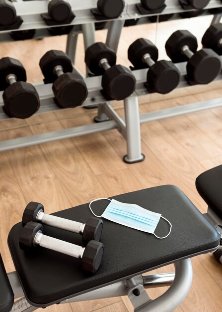 Pesas y mascarilla médica en banco de gimnasio