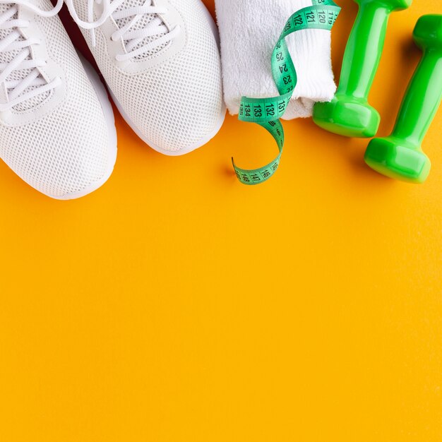 Pesas y zapatillas de deporte sobre fondo amarillo intenso con espacio de copia