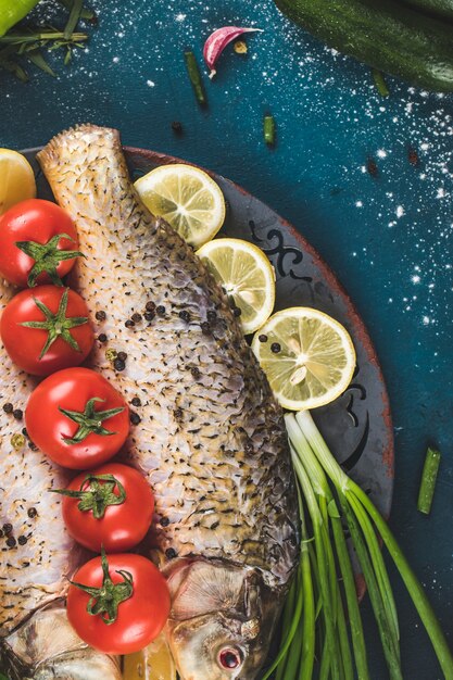 Pescado en una bandeja decorativa con limón, tomate y hierbas sobre una mesa azul