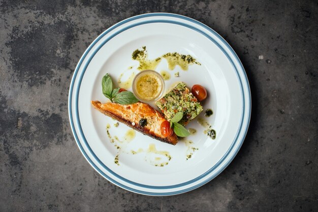 Un pescado cocido con salsa de tomates en una placa blanca.