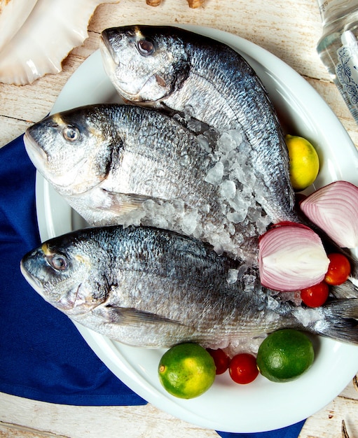 Foto gratuita pescado crudo colocado en un plato con cebolla lima, tomate cherry y hielo