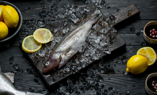 Pescado fresco en una tabla de madera con cubitos de hielo y limón