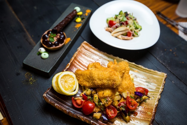 Pescado frito crujiente servido con berenjena frita y ensalada de tomate fresco