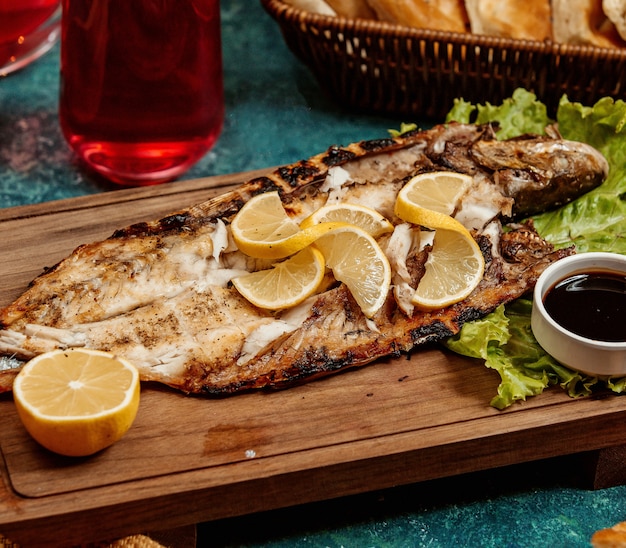 Pescado frito con rodajas de limón sobre una plancha de madera