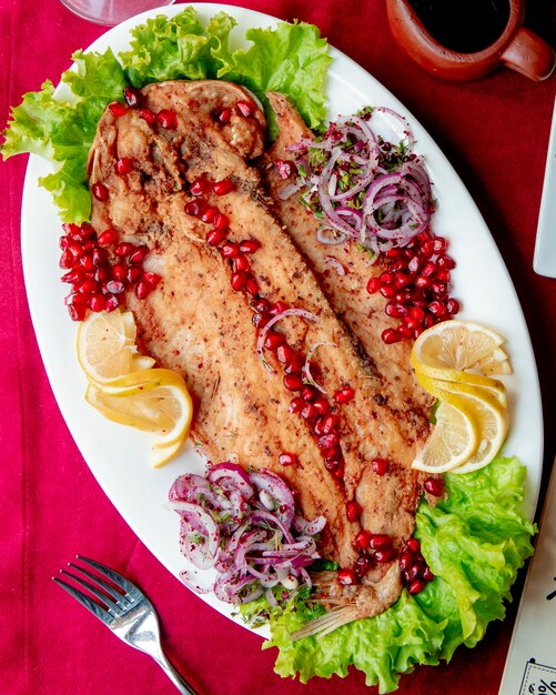 Pescado frito servido con lechuga granada, cebolla y rodajas de limón