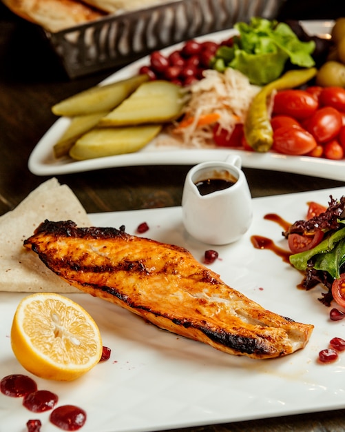 Foto gratuita pescado frito servido con salsa de limón, ensalada y pepinillos