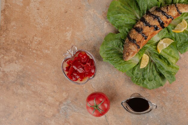 Pescado frito sobre lechuga con rodajas de limón, encurtidos y salsa de granada.