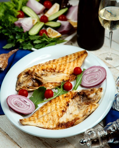 Pescado a la parrilla medio cortado servido con cebolla y tomate cherry