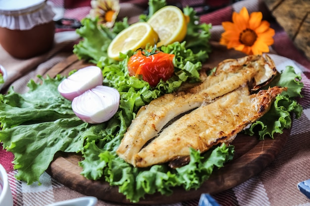 Foto gratuita pescado a la plancha en la tabla de madera cebolla lechuga tomate limón