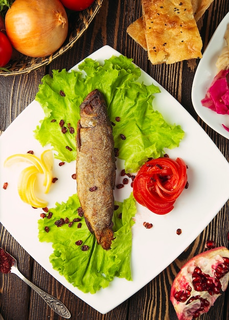 Pescado plateado a la parrilla servido con semillas de limón, lechuga, tomate y granada.