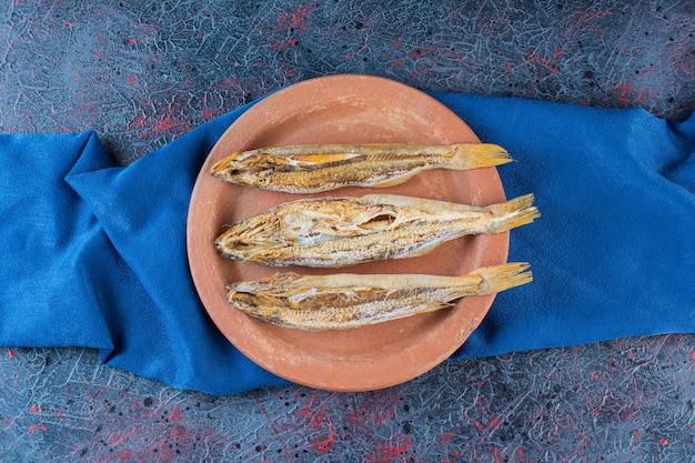 Foto gratuita pescado seco salado aislado en una placa de arcilla sobre un fondo oscuro.