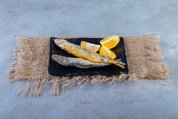 Pescado seco salado y rodajas de limón en un plato sobre una servilleta de arpillera, sobre la superficie de mármol.