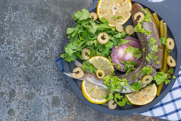 Pescado y verduras en una sartén de madera, sobre un paño de cocina.
