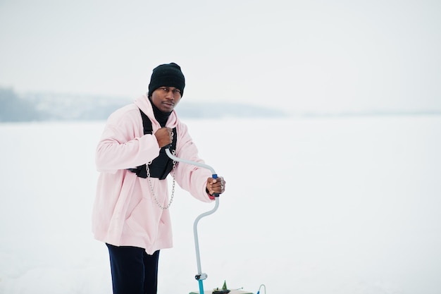 Pescador afroamericano haciendo un agujero en el hielo congelado con un taladro Pesca de invierno