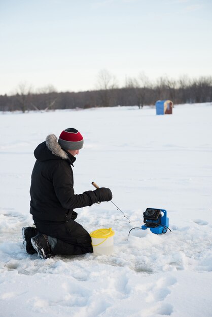 Pescador de hielo pescando en paisaje nevado