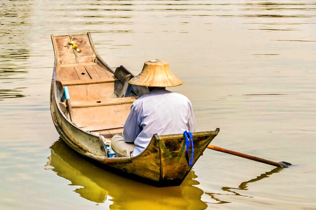 Pescador con un sombrero de cono asiático navegando en el lago con un pequeño bote de madera