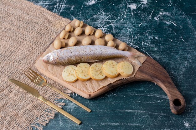 Pescados enteros crudos con aceitunas y rodajas de patata hervida sobre tabla de madera.