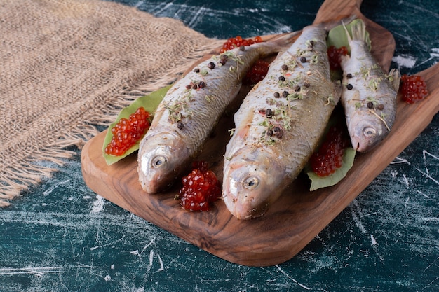 Pescados enteros crudos con caviar rojo sobre tabla de madera.