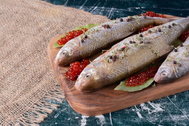 Pescados enteros crudos con caviar rojo sobre tabla de madera.