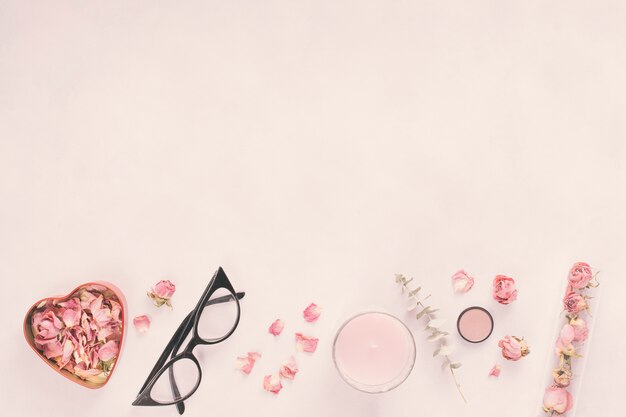 Pétalos de rosa con gafas y vela en mesa.