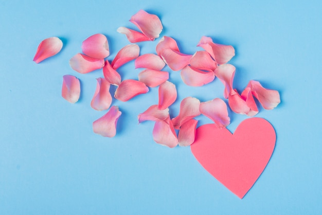 Pétalos de rosas con corazón rosa en la mesa.